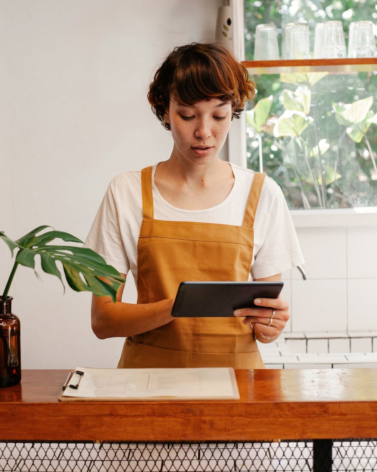 Empleada de una cafetería consulta una tablet detrás del mostrador.